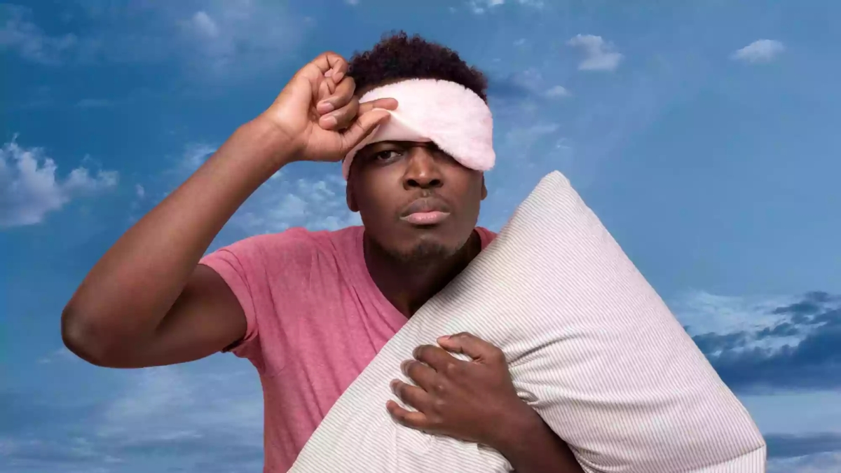Picture of man holding a pillow, starting to take off his blindfold